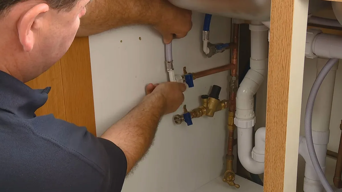 Plumber working on shutoff valves below a residential sink in a custom home